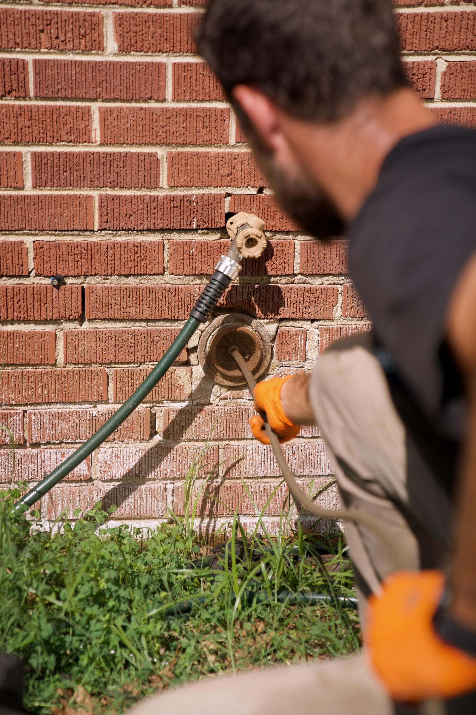 Technician hydro jetting a drain pipe at an exterior brick wall access point