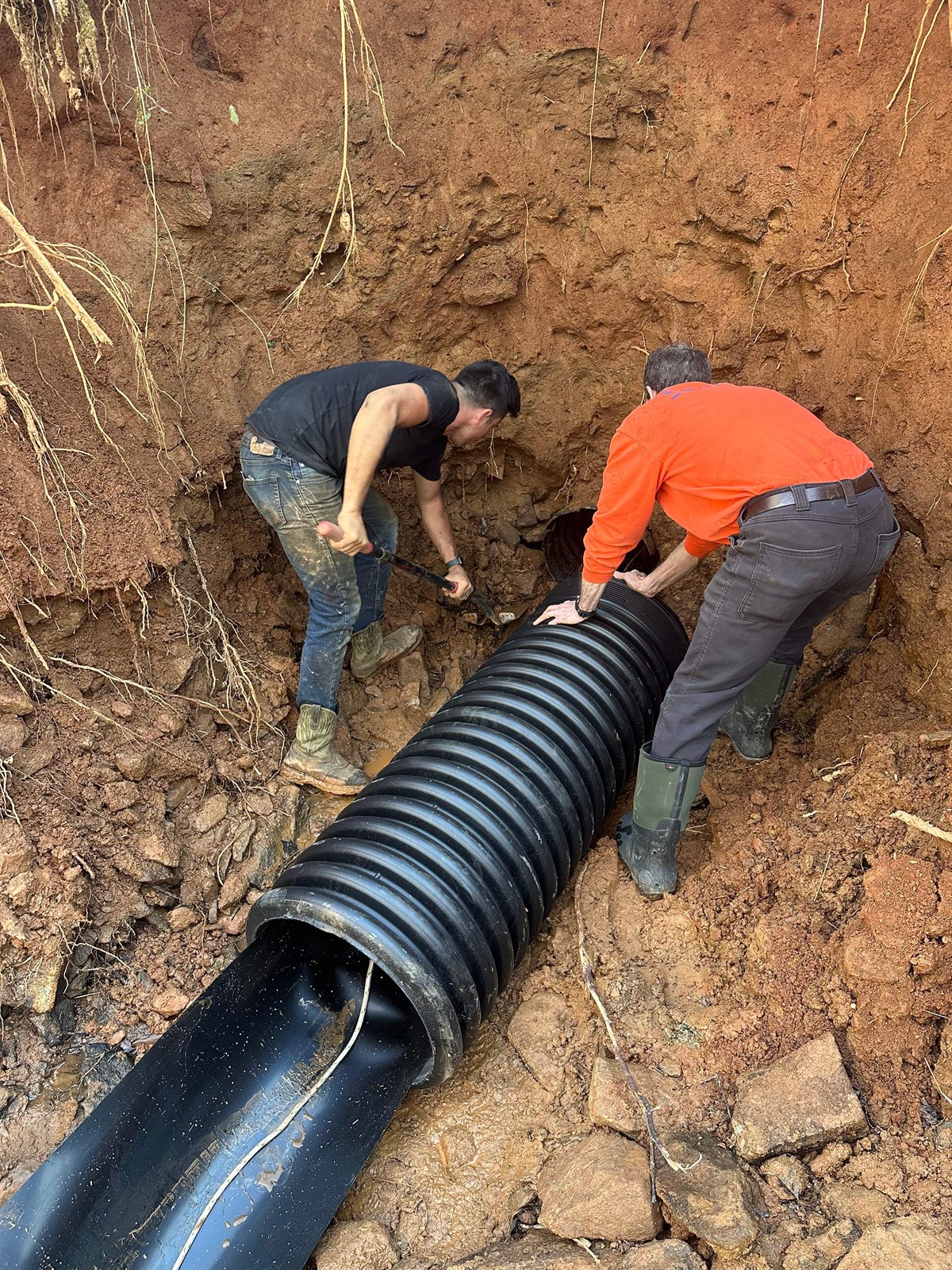 LiningWorks crew installing a corrugated storm drain pipe in an open trench.