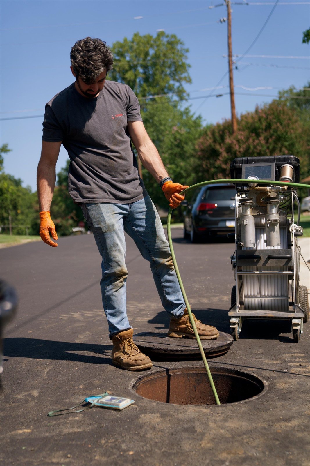 LiningWorks technician feeding a hydro jetting hose into a street manhole to clean a storm drain line.