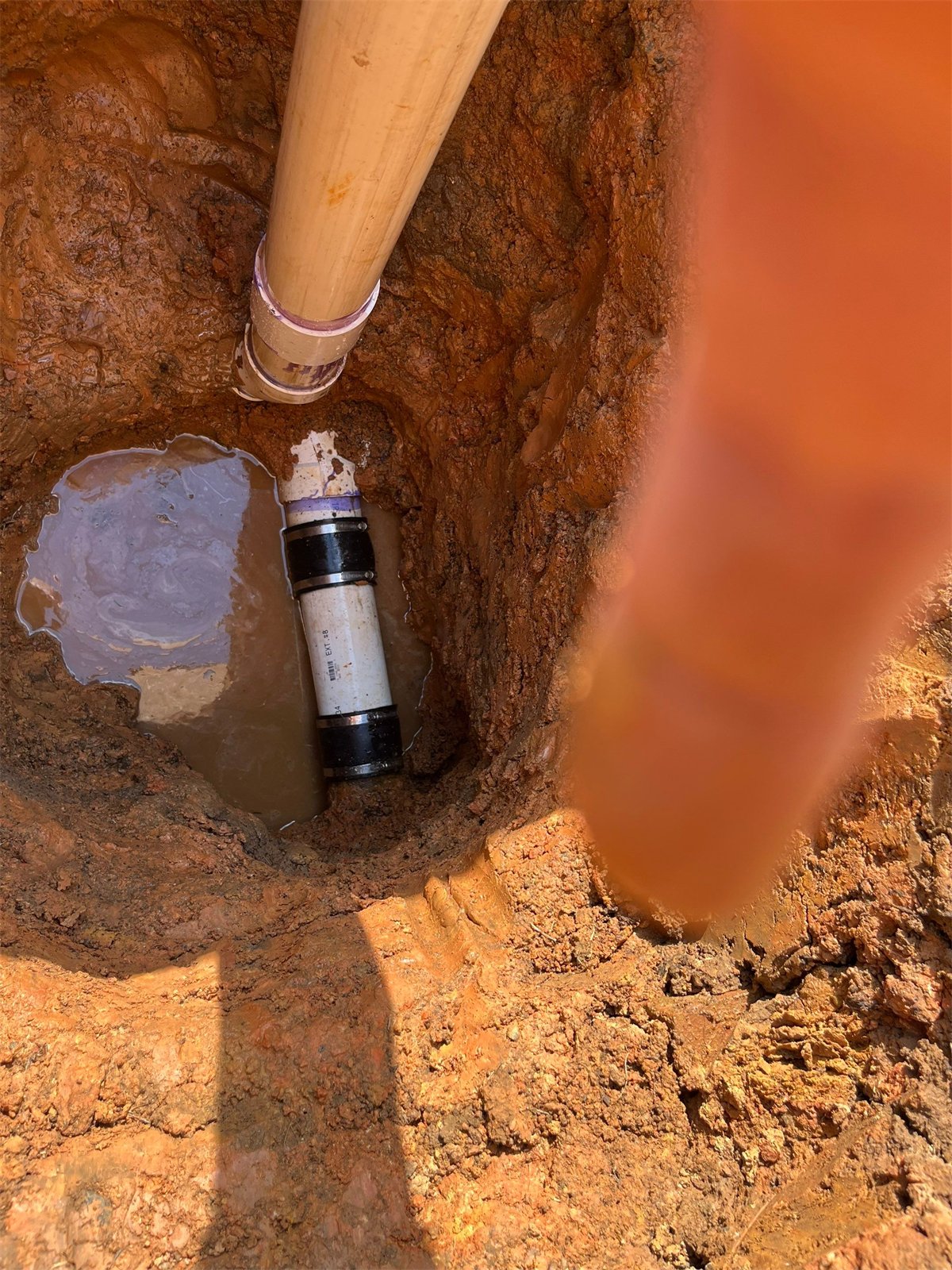 LiningWorks repairing an underground pipe connection in an excavation with standing water.